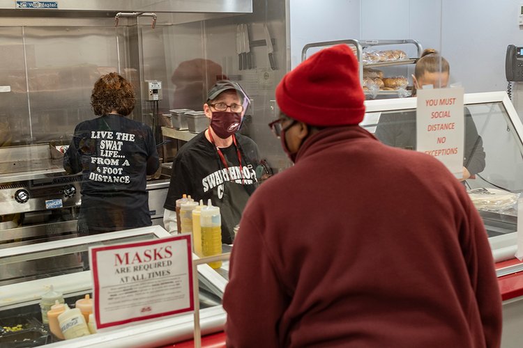 戴着口罩的人站在有机玻璃后面，为烧烤店的顾客点菜