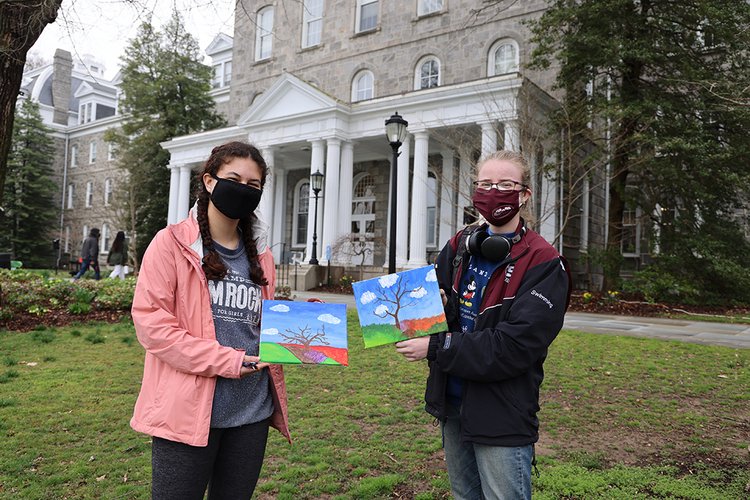 两个戴着口罩的学生举着光秃秃的树的画。
