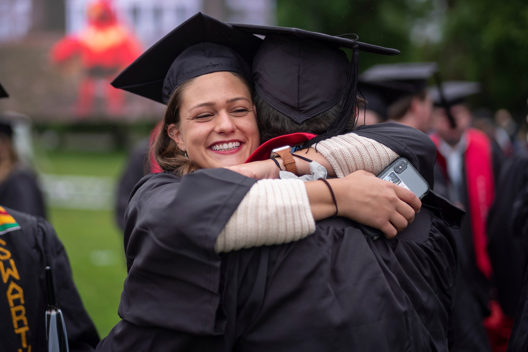 学生穿着毕业袍，戴着毕业帽，拥抱他人
